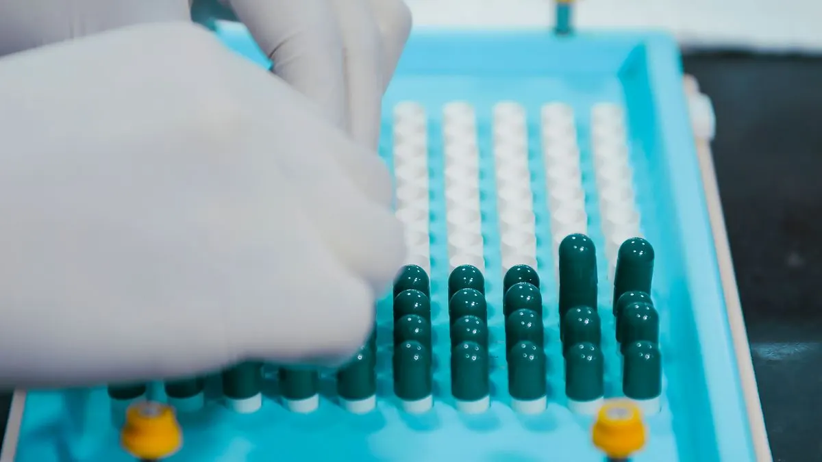 Gloved hands arranging capsules on a sterile tray during an aseptic material transfer step covered by the contamination control strategy