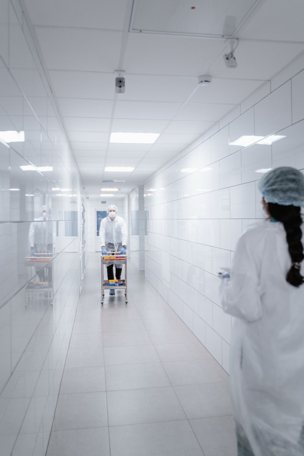 Opérateurs pharmaceutiques habillés déplaçant un chariot de flacons d'échantillons dans un couloir de salle blanche entre deux sas