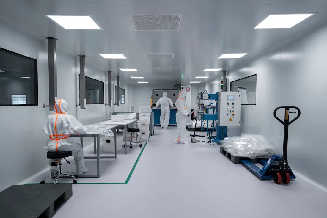 Operators in white coveralls working in an ISO 7 pharmaceutical cleanroom with a floor demarcation line