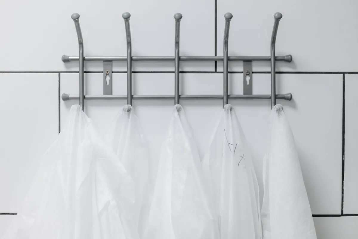 Tenues blanches de salle blanche suspendues à des patères dans un vestiaire carrelé