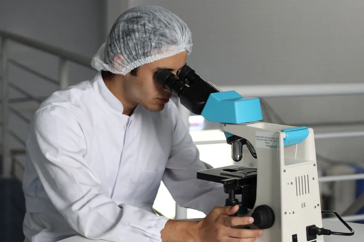 Microbiólogo con gorro examinando al microscopio una muestra de monitorización ambiental